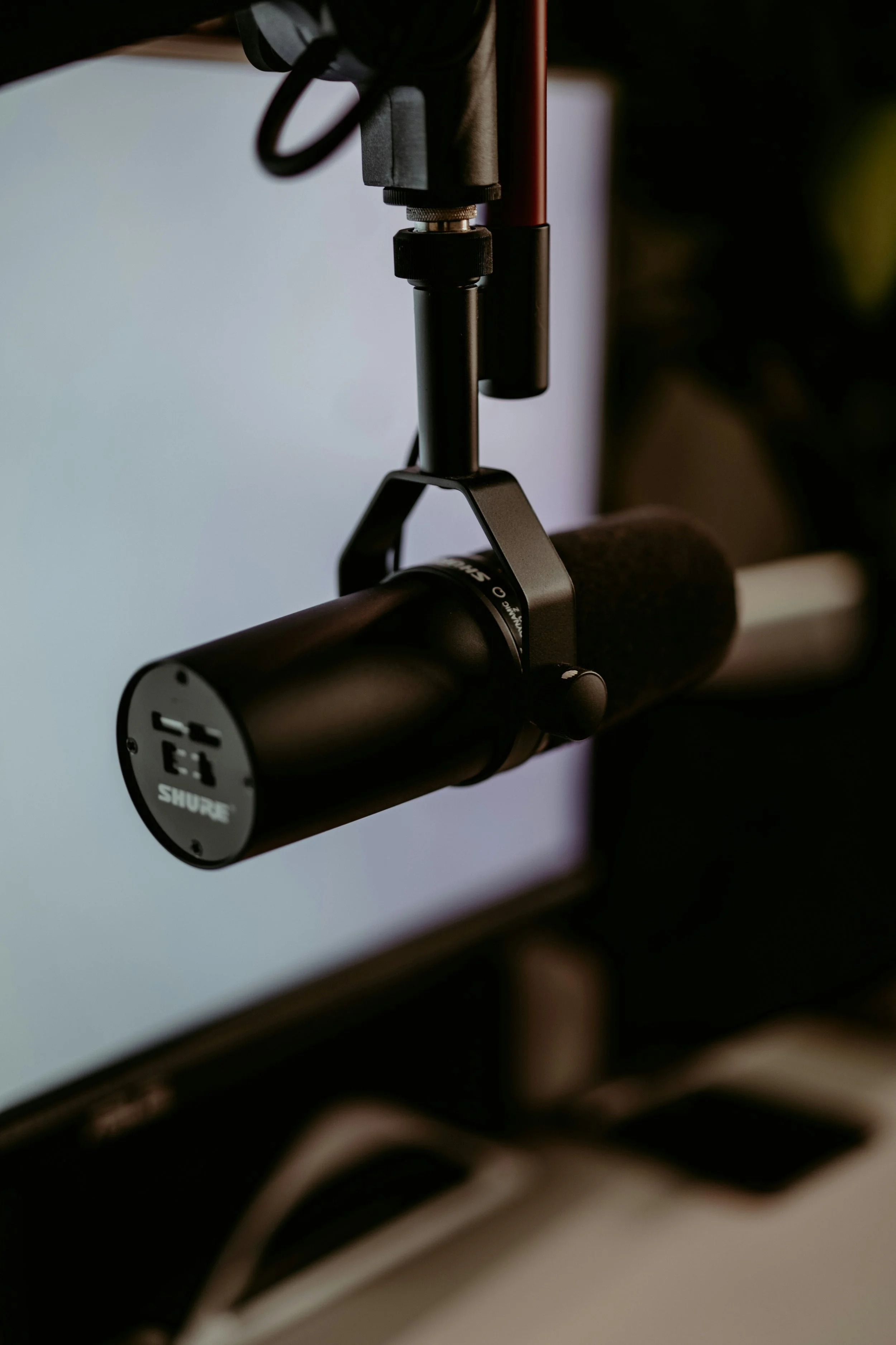 Close-up of a black Shure microphone mounted on a stand in front of a computer monitor.