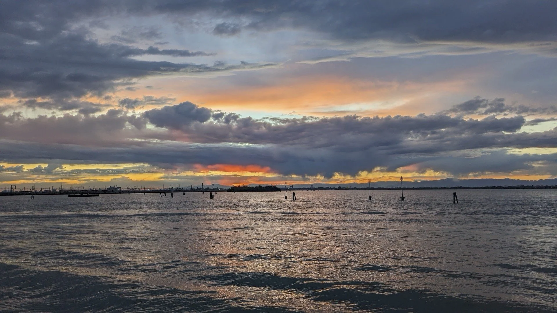 Sunset over a body of water with clouds in the sky and distant shoreline.
