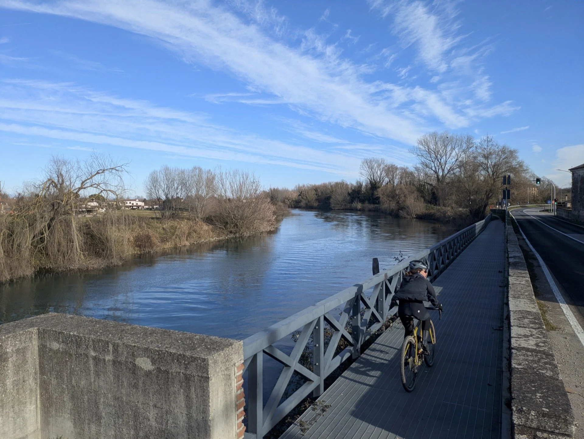 A person riding a bicycle on a bridge over a river with clear blue skies and leafless trees.