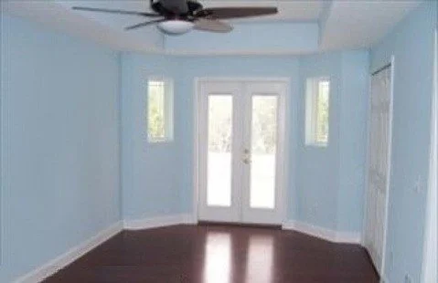 Empty light blue room with double doors leading outside, ceiling fan, and windows