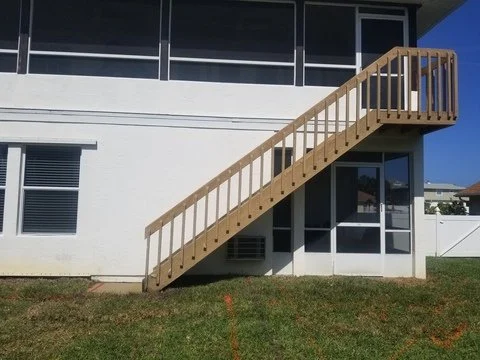 Wooden outdoor staircase leading from a second floor to the ground level of a white building.