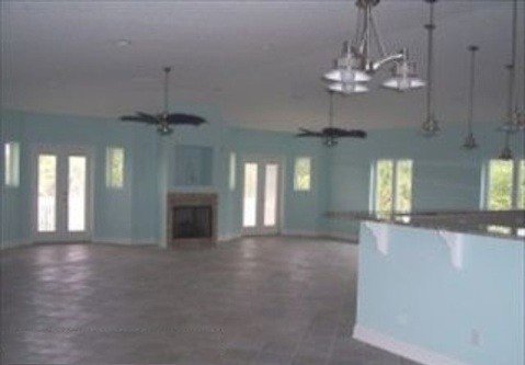 Empty living room with multiple windows and a fireplace, ceiling fans, and a partial kitchen counter visible.