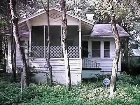 A small house with a screened porch, surrounded by trees and greenery.