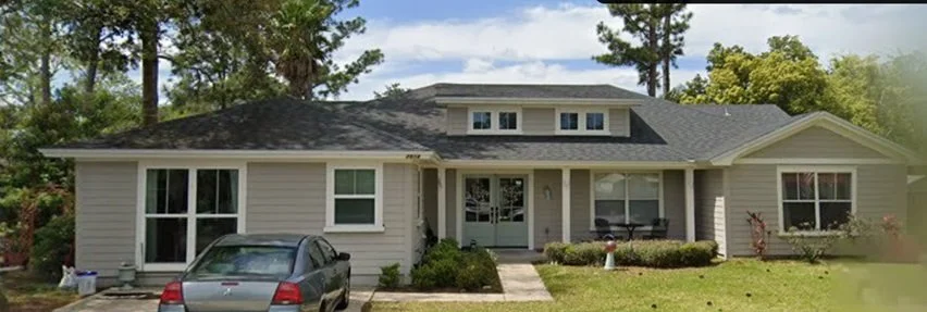 Front view of a suburban house with a driveway, parked car, and well-maintained lawn with shrubs and trees.