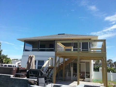Back view of a two-story house with a balcony and wooden stairs leading to the backyard.