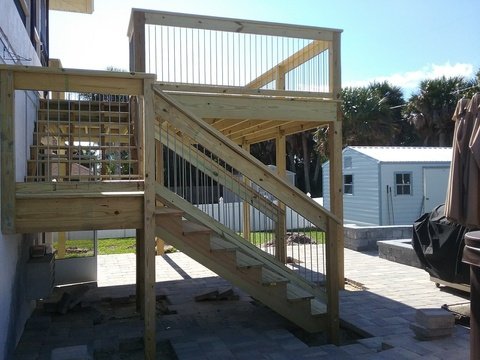A wooden staircase leading up to a second-story deck with a railing in a residential backyard.