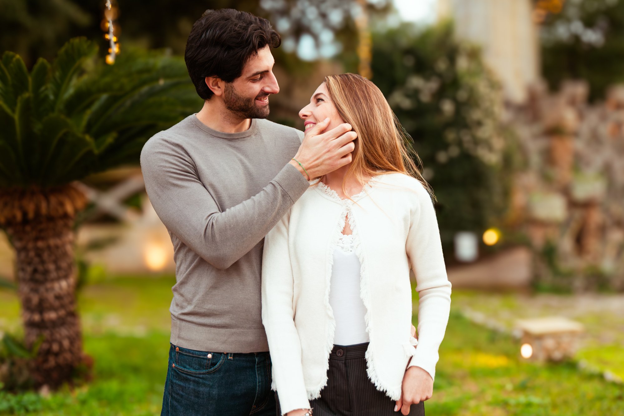Un uomo e una donna si sorridono affettuosamente all'aperto, con l'uomo che tocca il viso della donna.