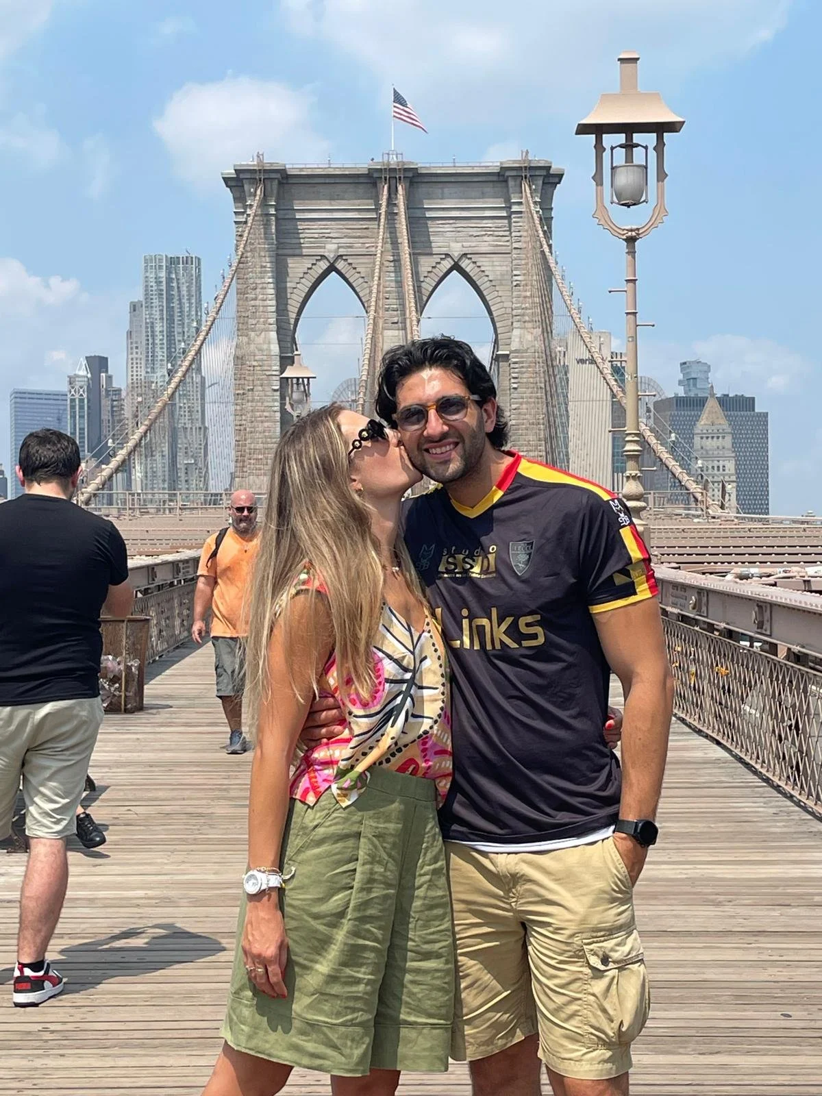 Una coppia si abbraccia e si scambia un bacio sulla fronte sul ponte di Brooklyn a New York, con il skyline e l'Empire State Building sullo sfondo.
