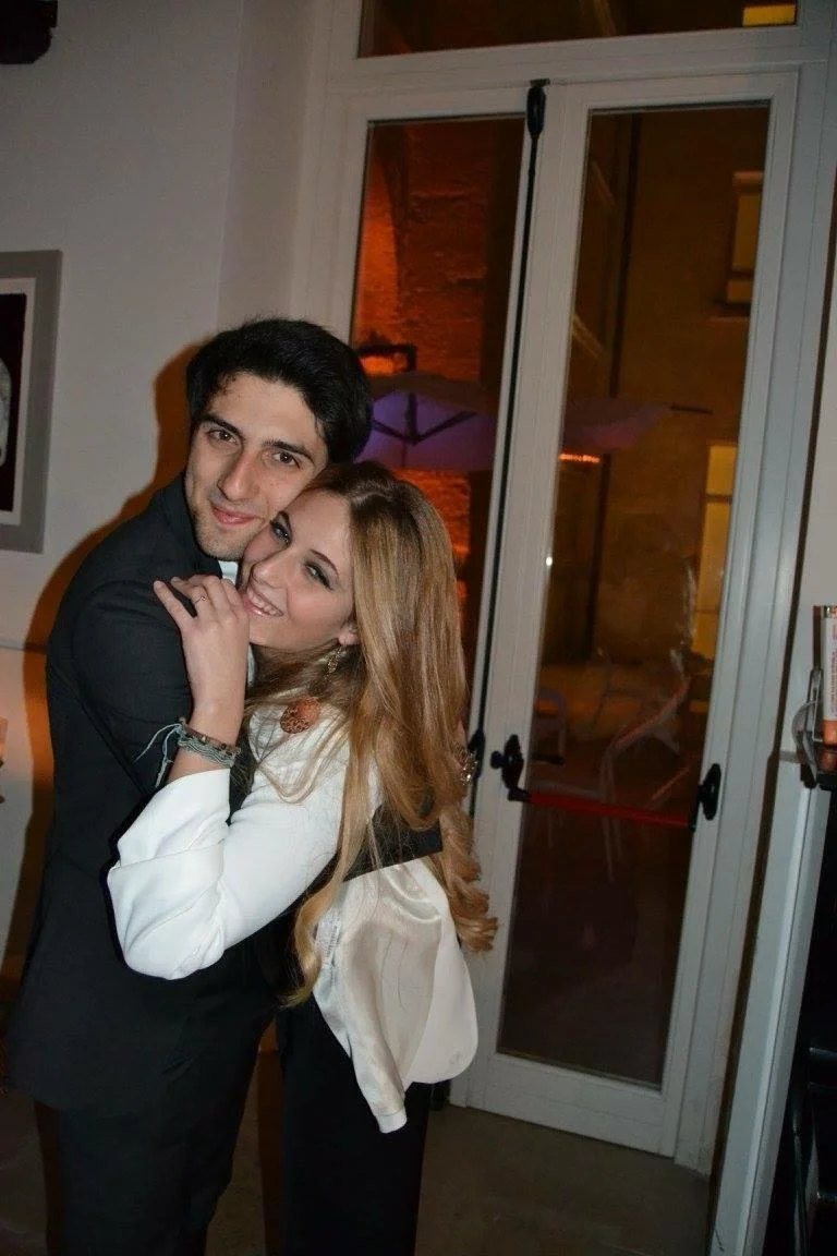 Una coppia di giovani si abbraccia e sorride davanti a una porta vetrata in un ambiente interno con luce calda