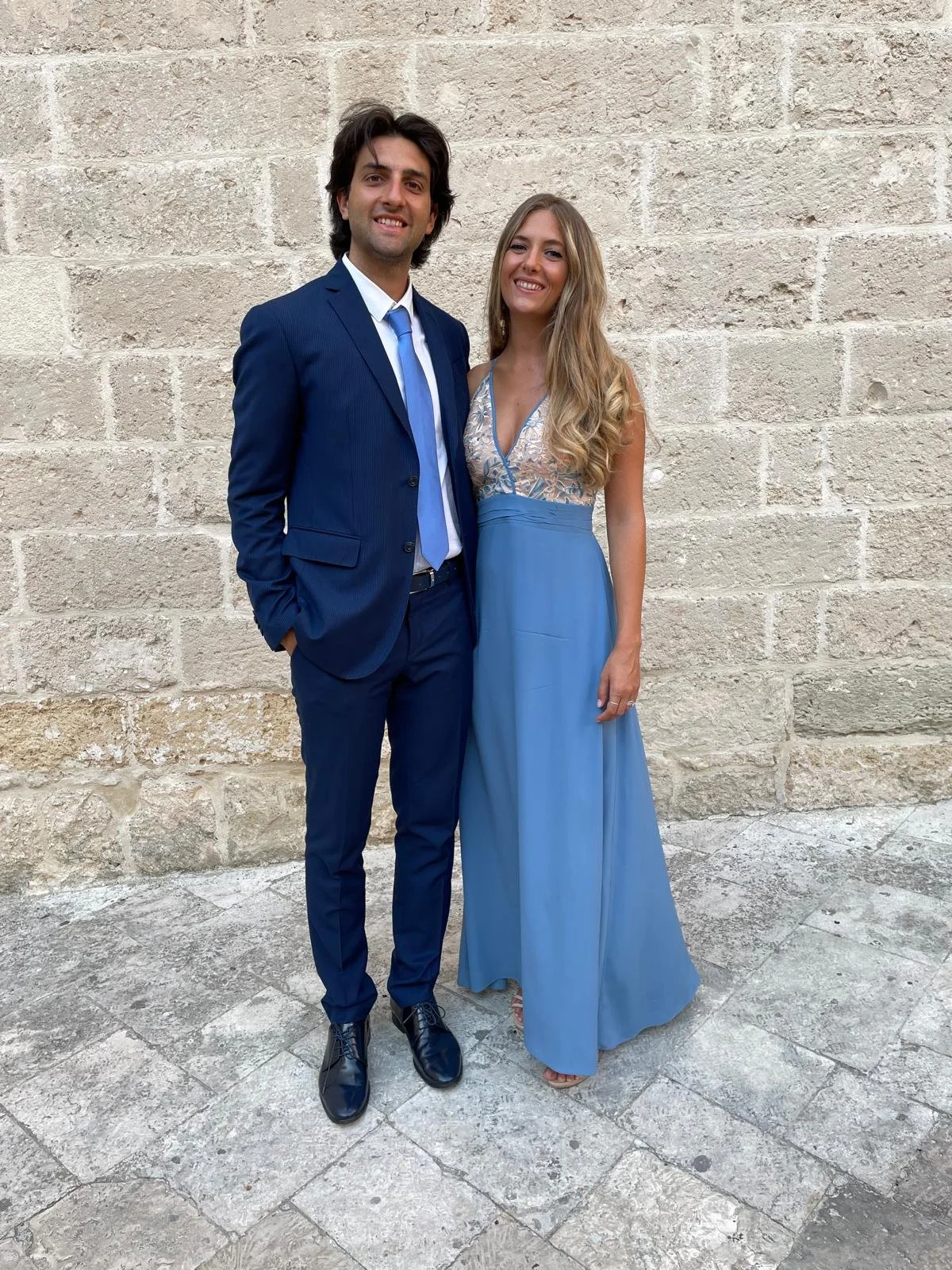 Una coppia vestita elegantemente davanti a un muro di pietra