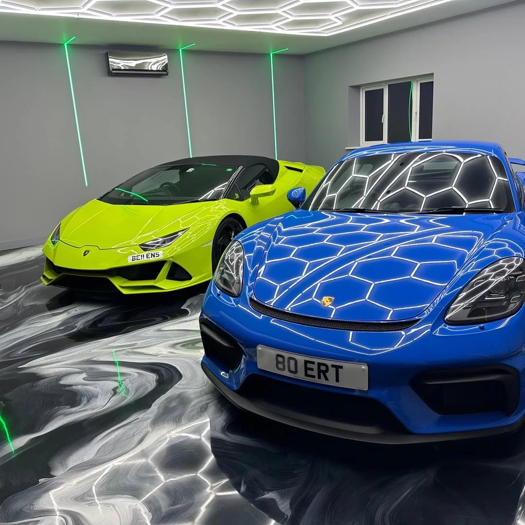 Two luxury sports cars, a bright green Lamborghini and a blue Porsche, parked in a modern garage with LED lighting and reflective marble floors.