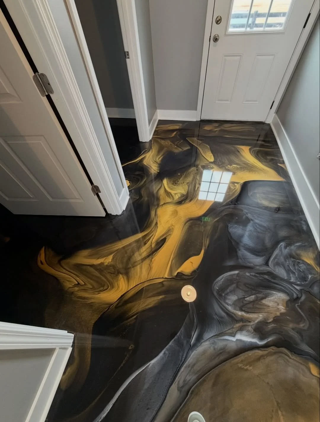 Interior of a house entryway with a striking black, gold, and gray marbled epoxy flooring reflecting a window and ceiling light.