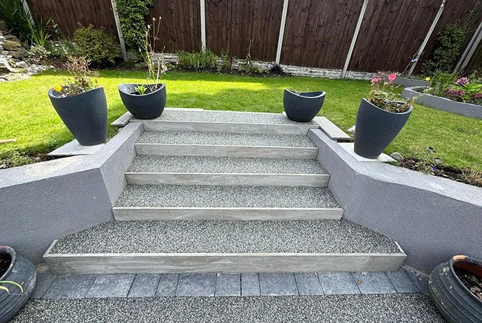 Concrete stairs leading up to a backyard garden with potted plants and a wooden fence.