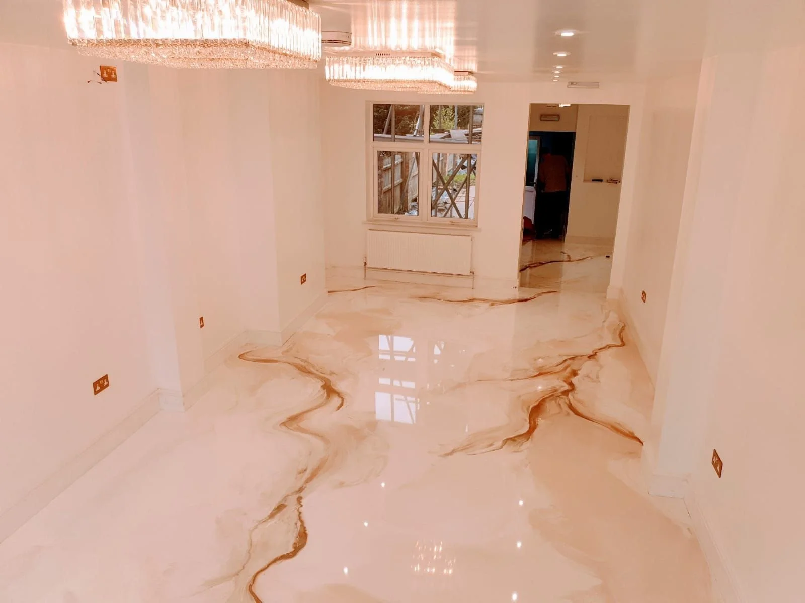 Empty room with glossy marble floor featuring beige and brown veining, white walls, a chandelier, and a window with a view outside.