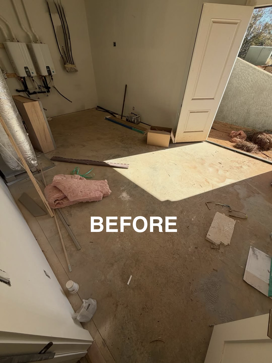 Empty room with construction tools and materials, an open door leading outside, and uninstalled flooring.