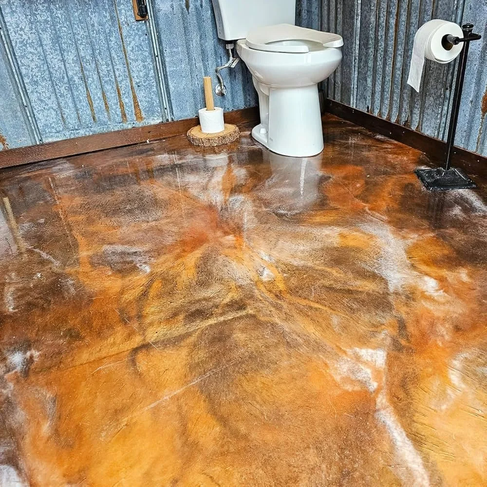 Rustic bathroom with blue corrugated metal walls, a white toilet, a black toilet paper holder with a roll of toilet paper, a wooden toilet brush holder, and a polished concrete floor with a marbled appearance.