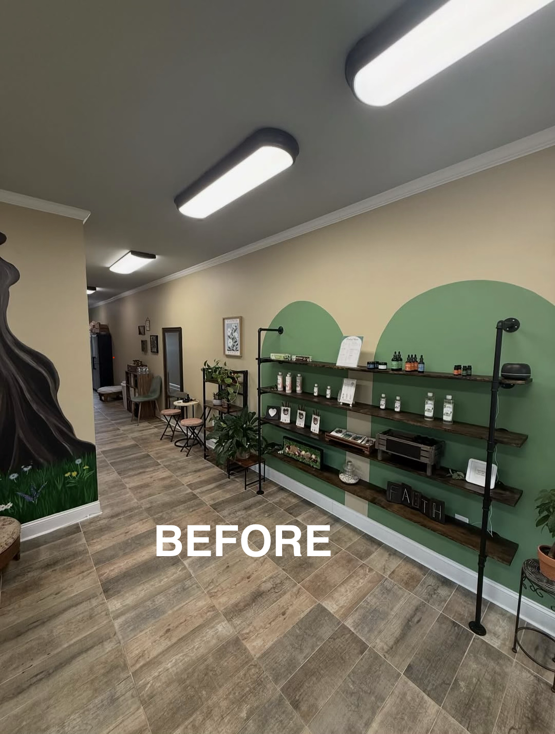 Interior view of a wellness or treatment room with wooden shelves displaying essential oils and skincare products, green wall accents, and seating area with chairs and plants, under ceiling lights, labeled 'BEFORE'.