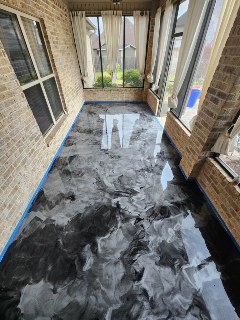 Sunroom with marbled black, gray, and white epoxy resin flooring, surrounded by brick walls, large windows with white curtains, and a view of a backyard.