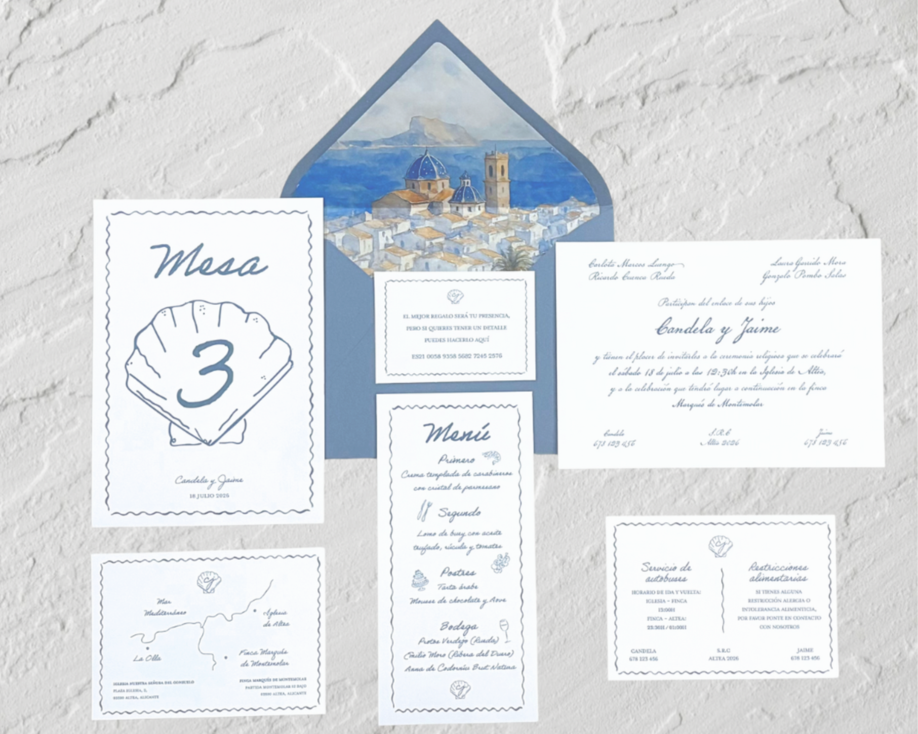 Invitación de boda y papelería en tonos azules y blancos, incluyendo un menú, una tarjeta de mesa y otra de actividades, acompañados de un sobre con vista pintada de un pueblo con iglesia y mar en el fondo.