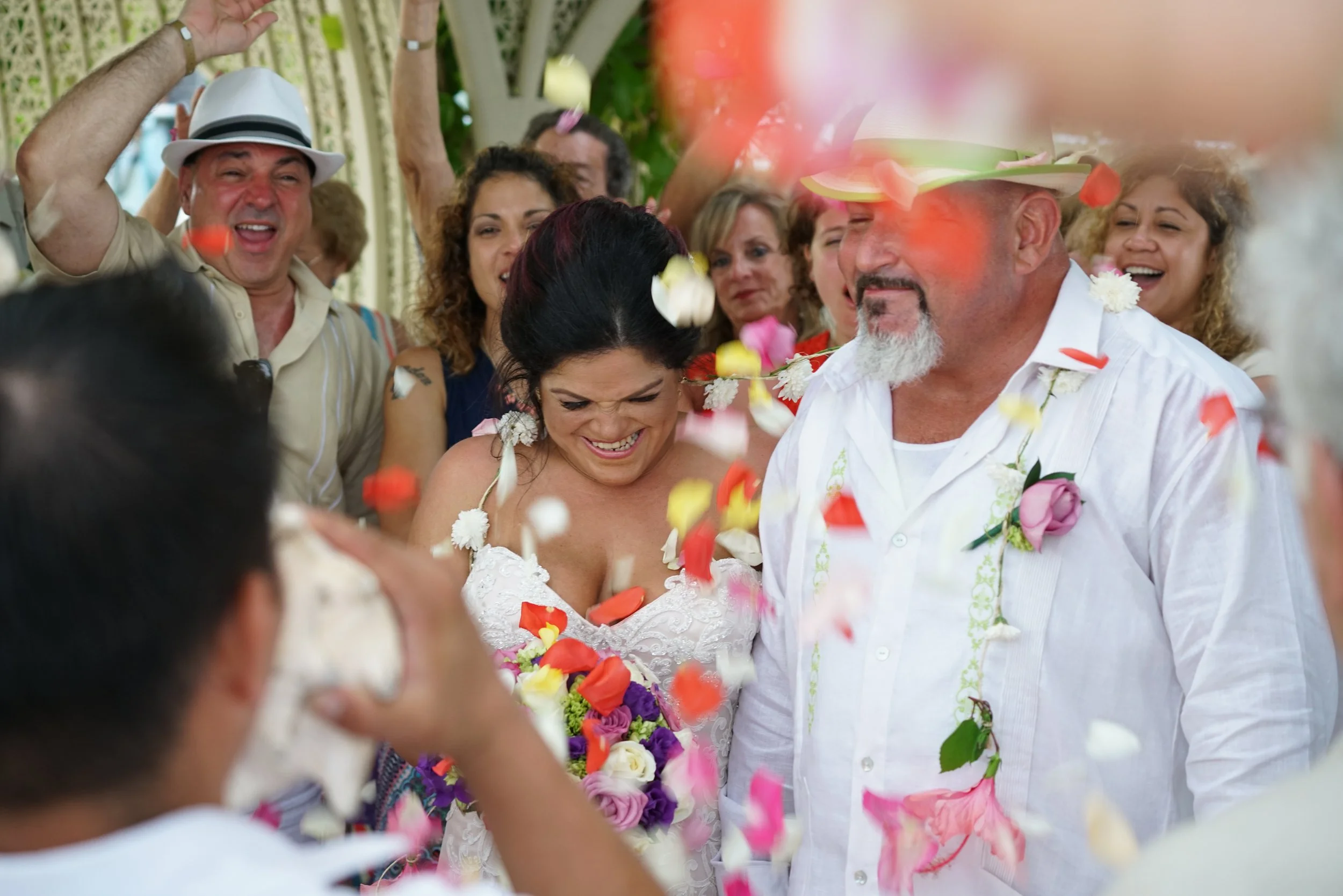 A wedding celebration with a bride and groom surrounded by friends, as flower petals are thrown in the air.