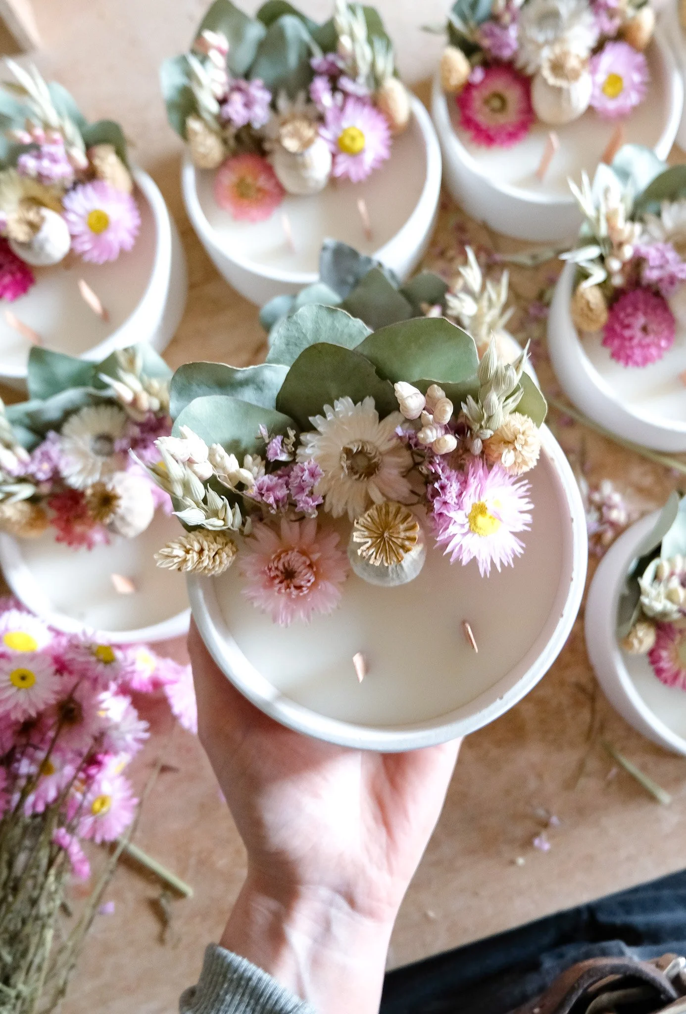 Bougie blanche décorée avec un arrangement florale de fleurs pastel, feuilles vertes et petites fleurs séchées.