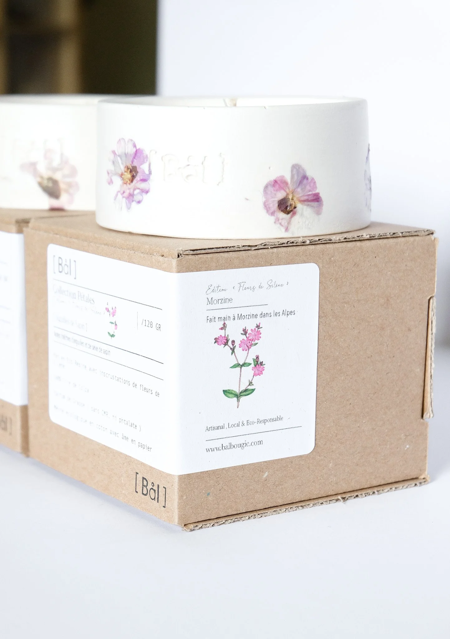 Un moule à gâteau en céramique blanc avec des fleurs pressées, posé sur une boîte en carton avec une étiquette qui montre une illustration de fleurs roses.