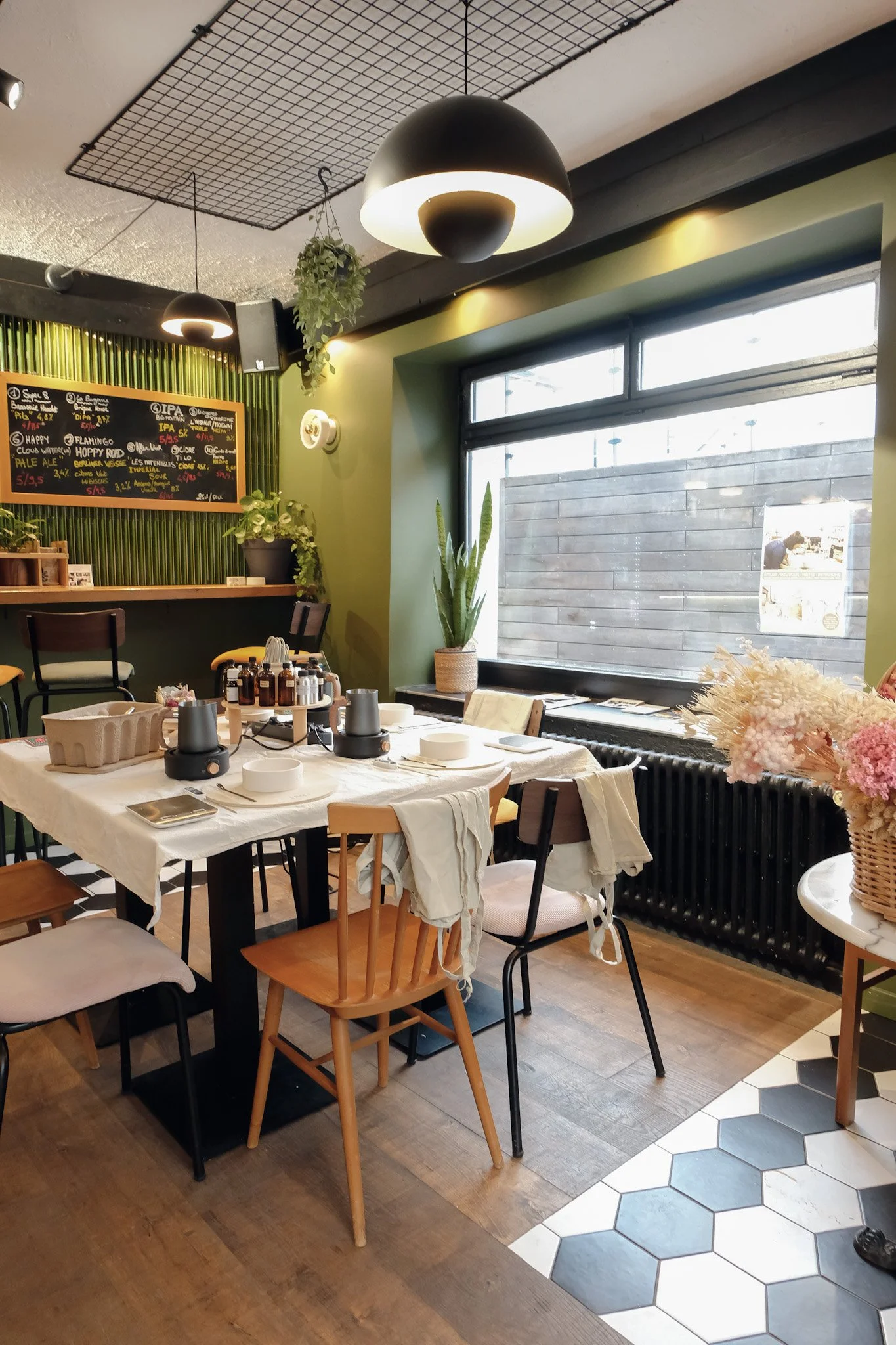 Intérieur d'un restaurant ou café avec une table dressée, des chaises, des plantes et un tableau noir avec dessins et écrits en arrière-plan.