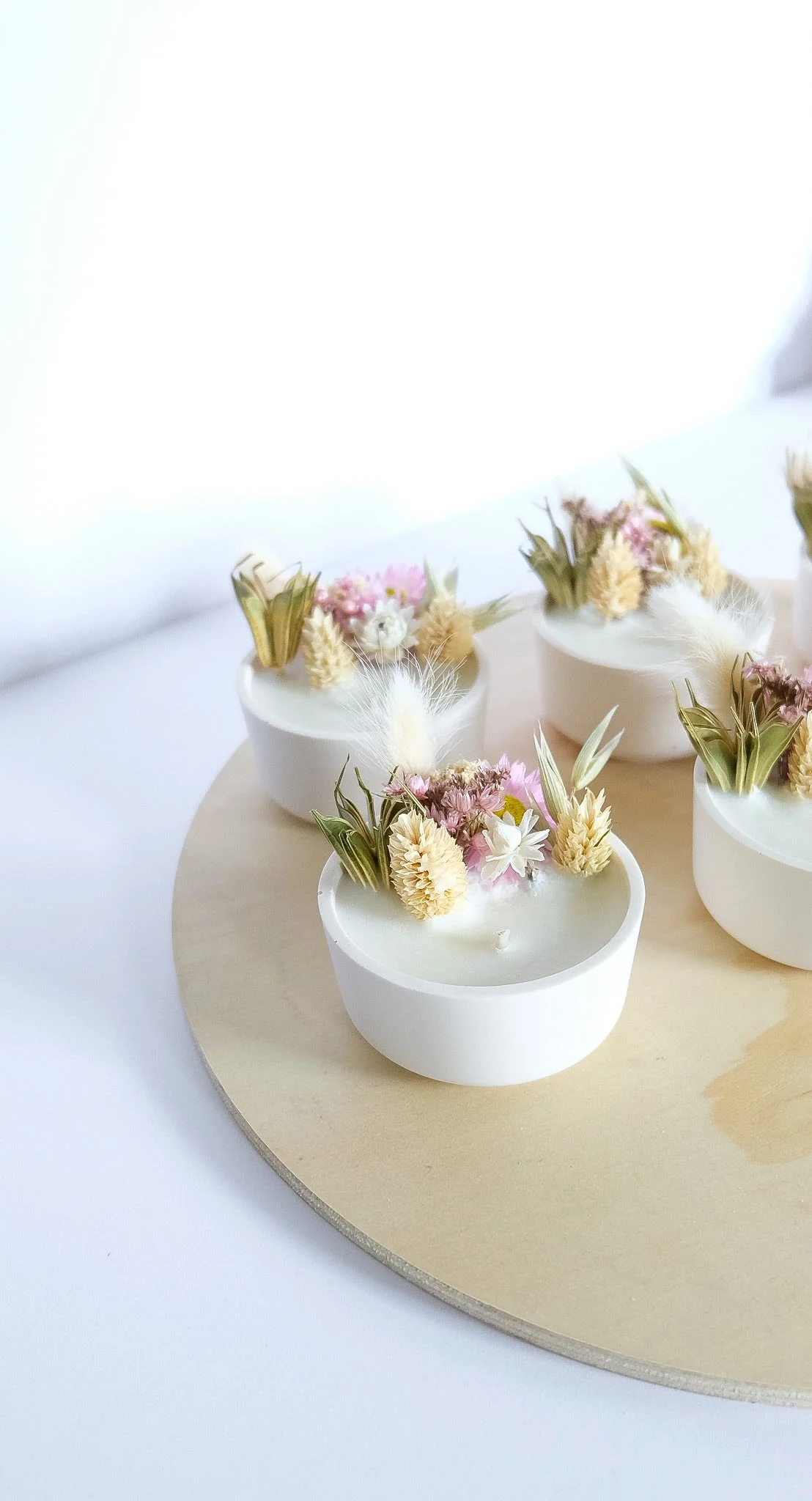 Bougies flottantes décoratives avec fleurs séchées dans des contenants blancs sur un plateau en bois