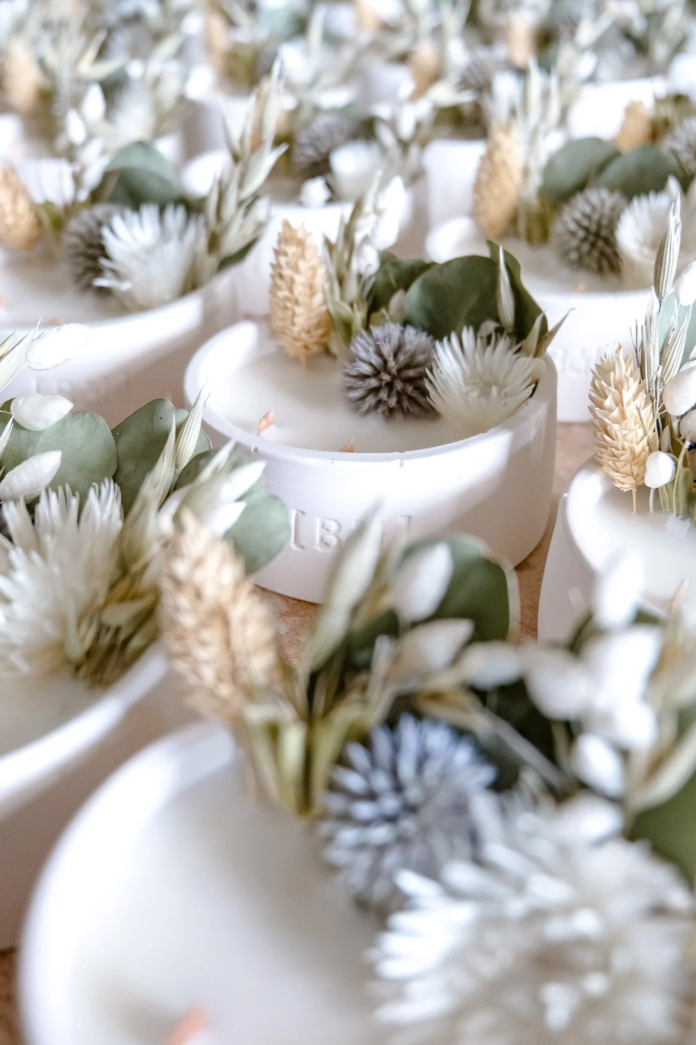 Bougies parfumées décoratives avec fleurs et feuilles sèches dans des contenants blancs.