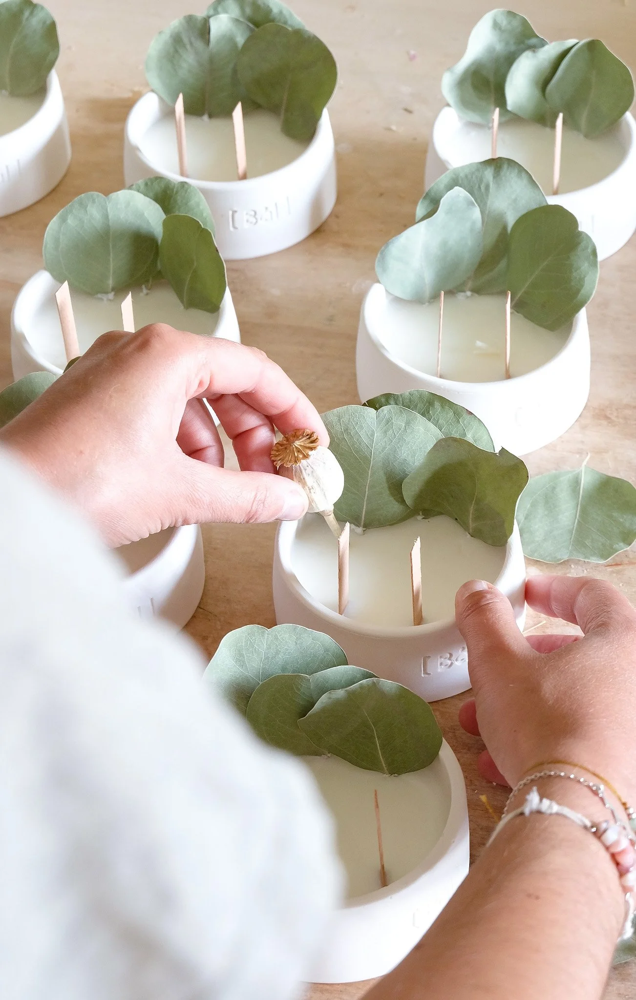 Mains décorant des bougies blanches avec des feuilles de eucalyptus dans des contenants blancs