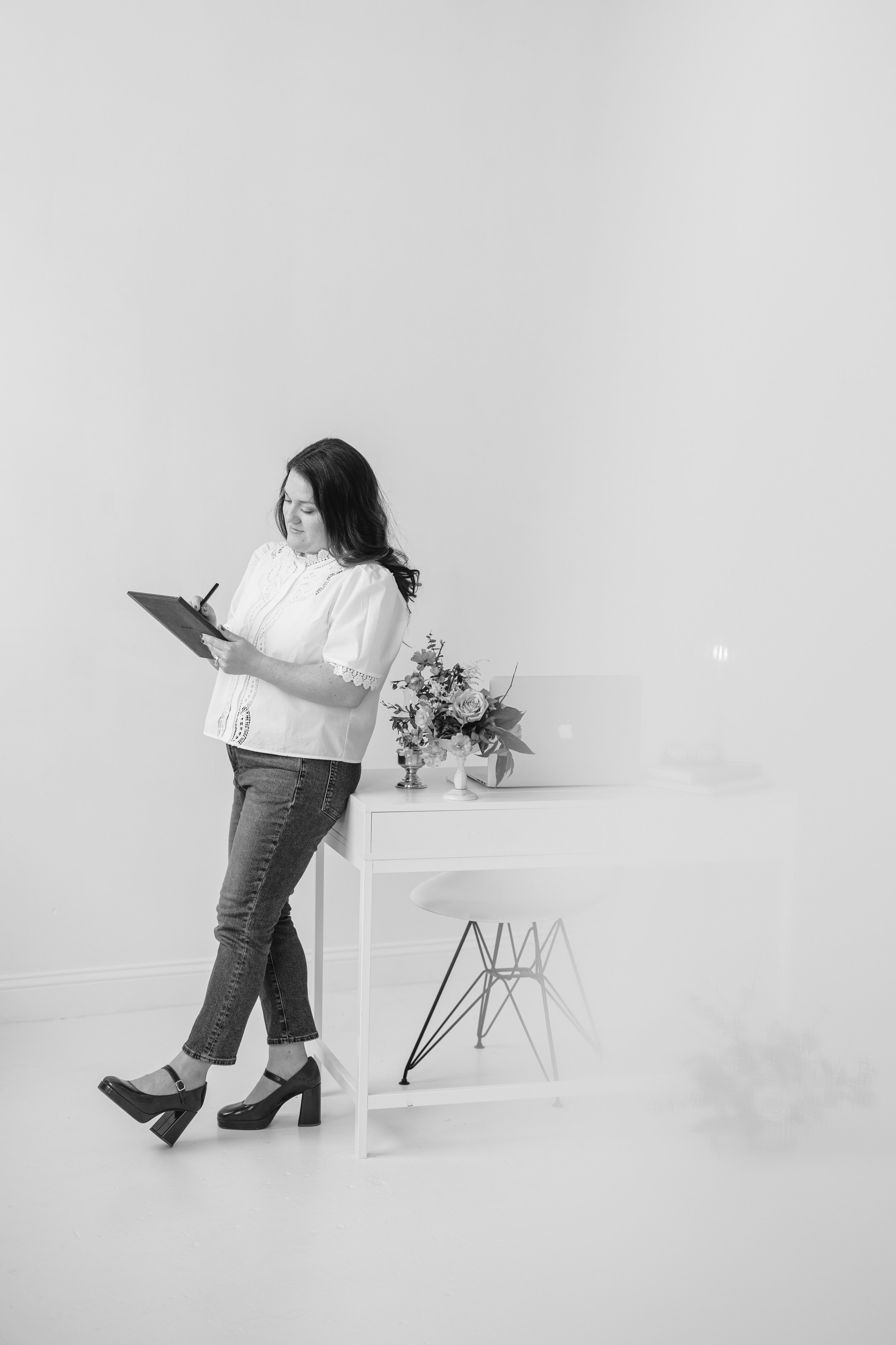 Woman holding a notebook, standing at a desk with a laptop, reflecting on responsibilities and mental load.