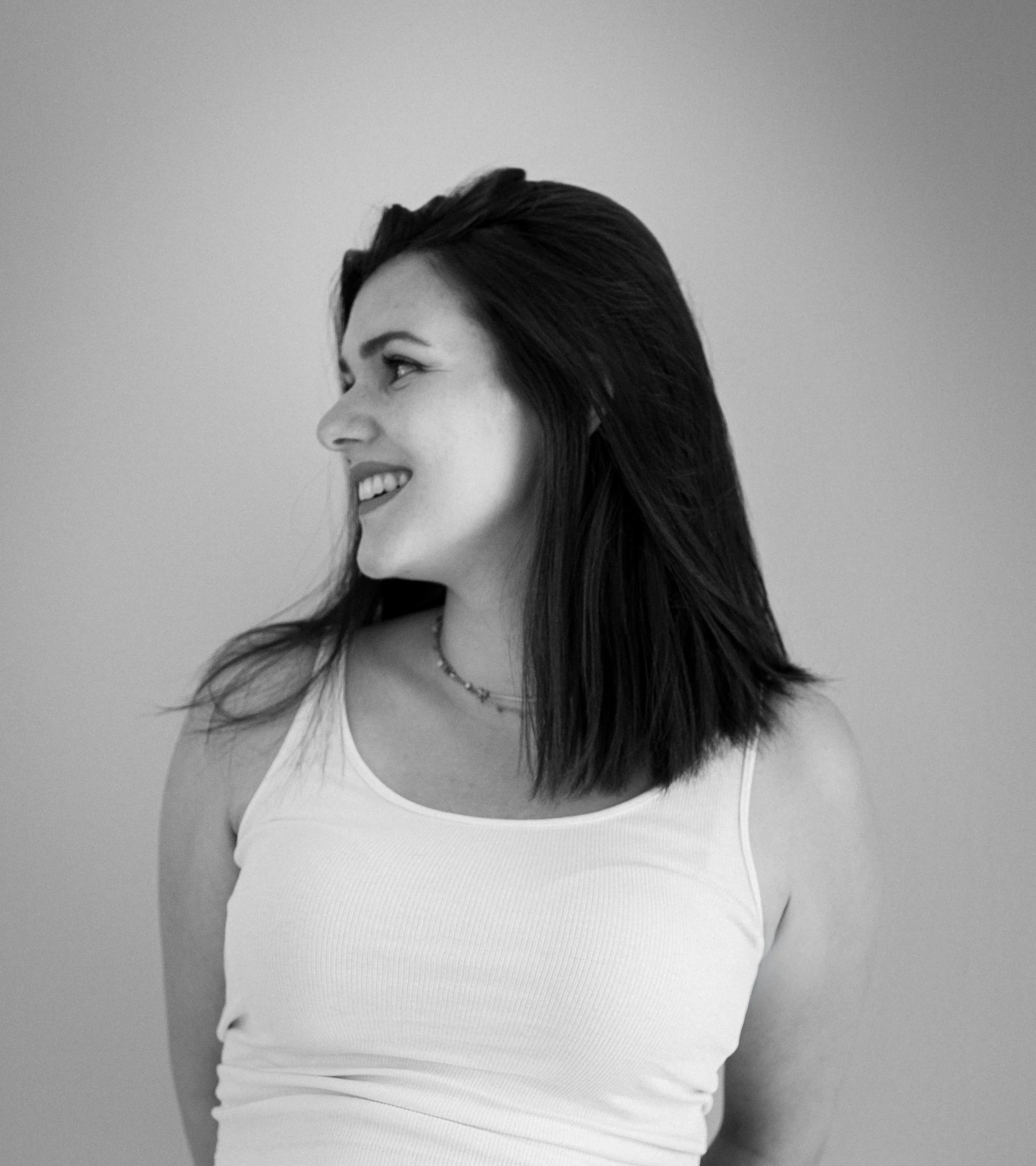 Schwarz-weiß-Foto eines lachenden jungen Mädchens in weißem Top, seitlich betrachtet, vor hellem Hintergrund.