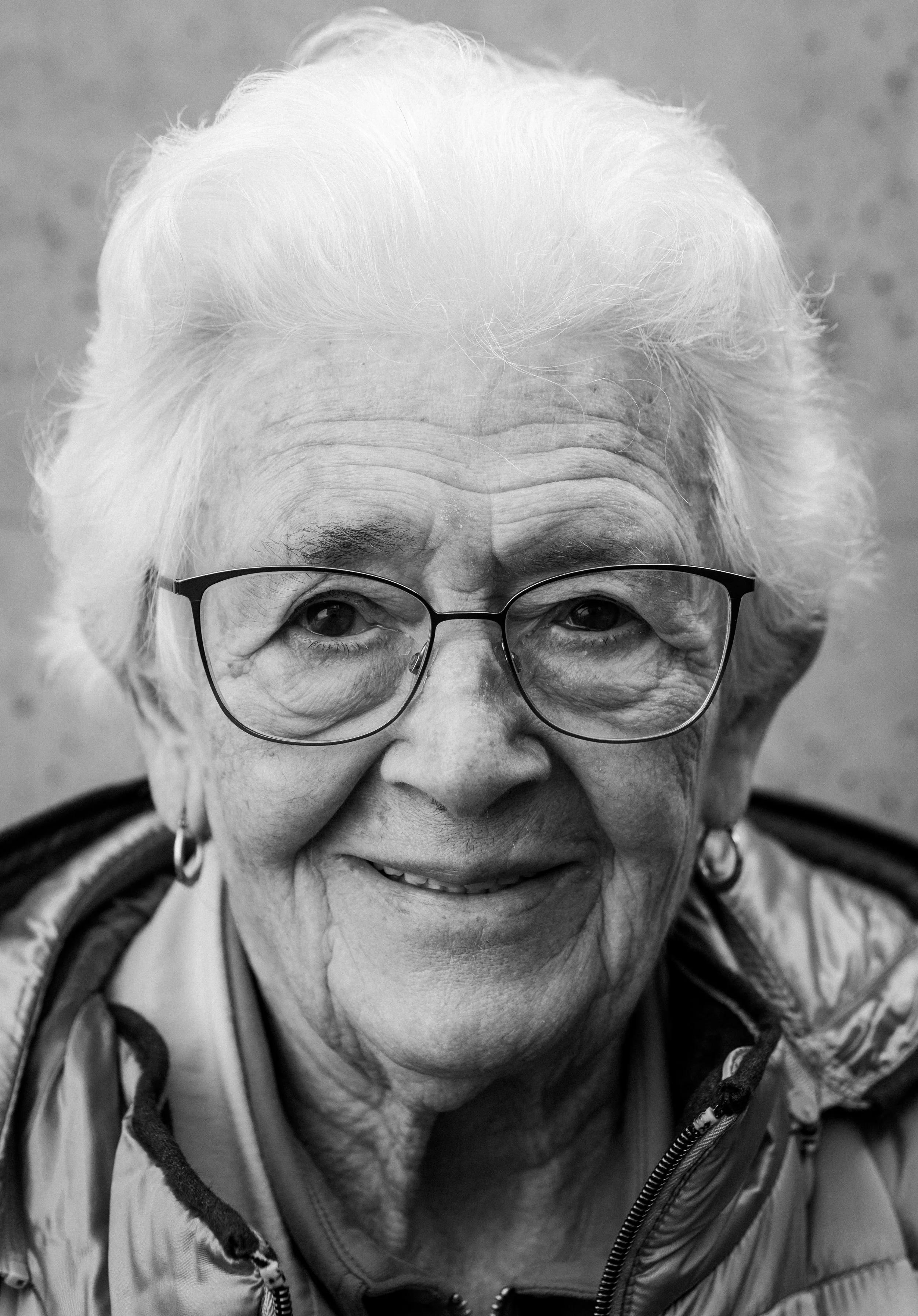 Ein alter Mensch mit weißen Haaren, trägt Brille und lächelt, aufgenommen in schwarz-weiß, Nahaufnahme.