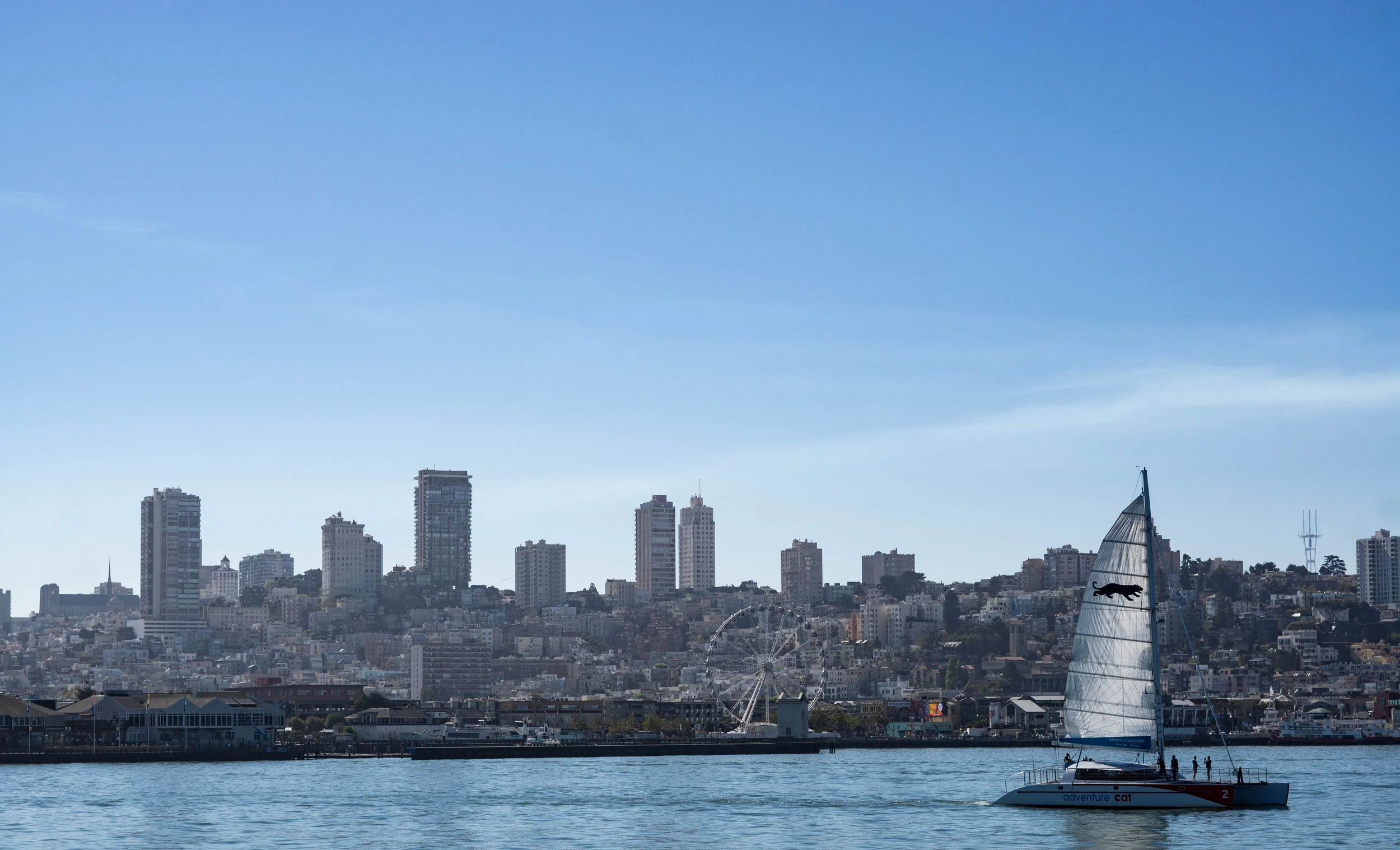 Stadtansicht mit Hochhäusern, ein Raddampfer und eine Segelyacht auf dem Wasser bei klarem Himmel.