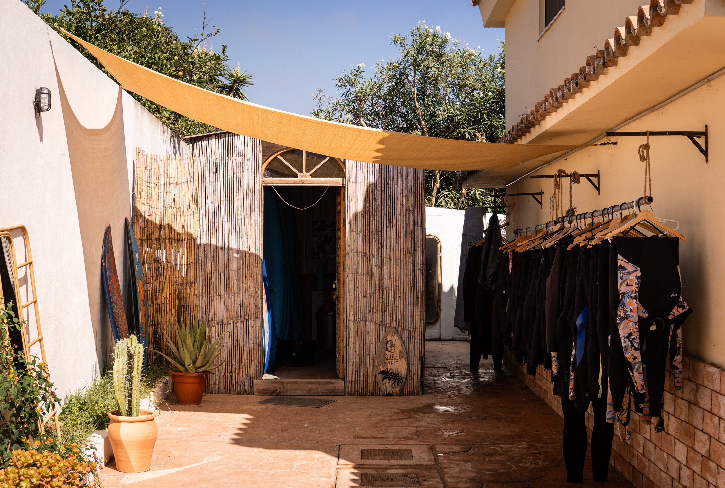 Sonnengeschützte Terrasse mit Wäsche zum Trocknen, Surfzubehör, Pflanzen und einer Holzhütte im Hintergrund