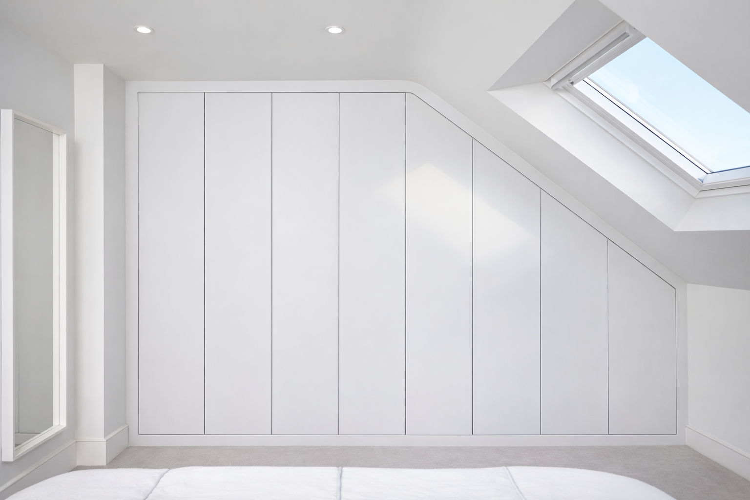 Empty white closet doors with sloped ceiling and skylight window in a bright, minimalist bedroom.