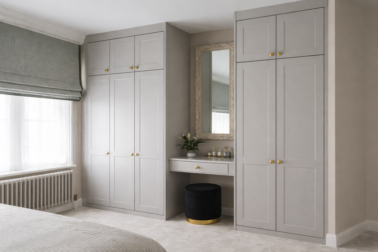 A bedroom corner with built-in gray wardrobes, a small vanity area with a mirror, a black stool with gold trim, a plant, and toiletries on a tray.