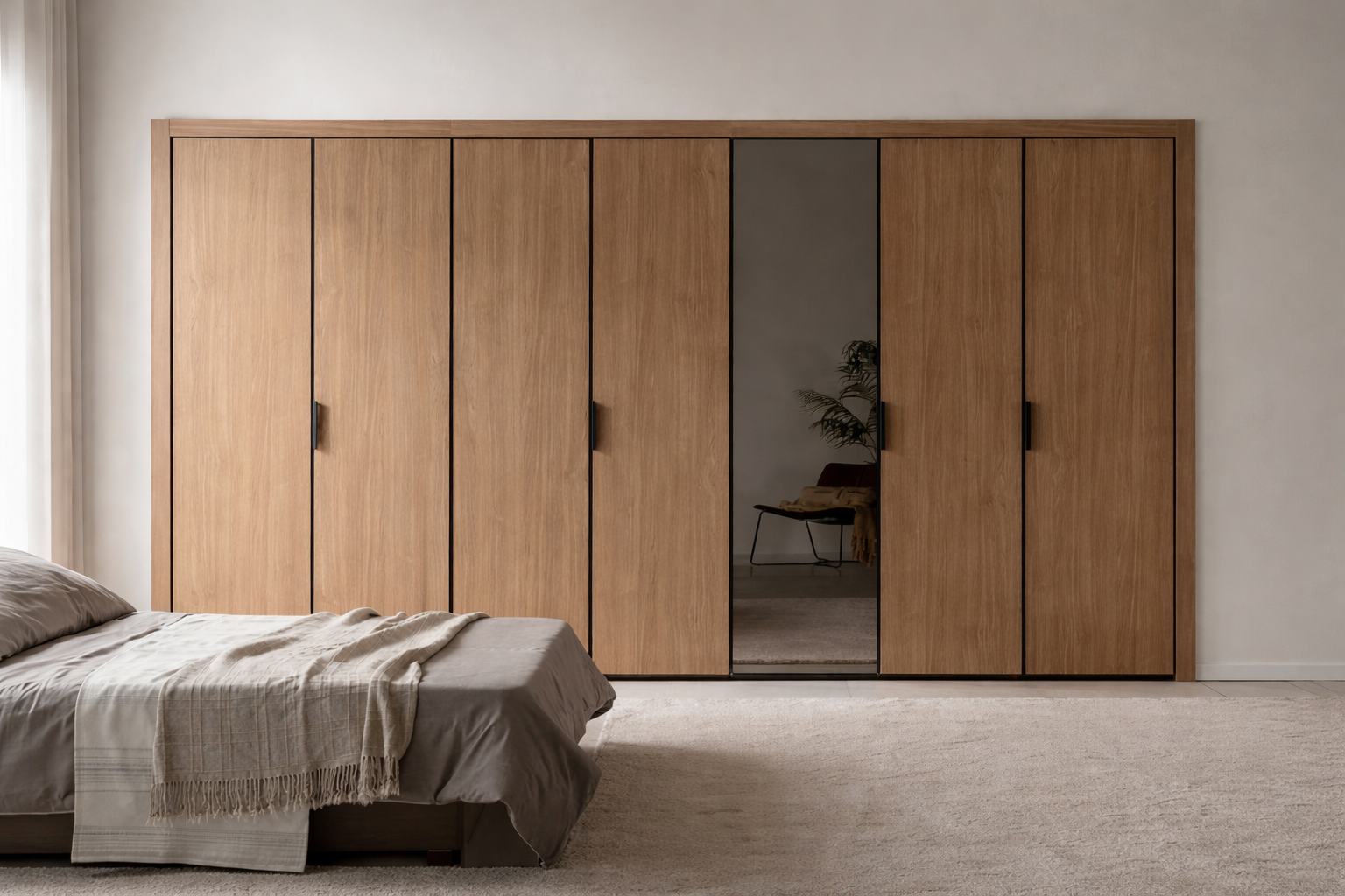 A bedroom with a large wooden sliding closet door, a bed with beige bedding and a blanket, and a mirror on the closet door reflecting a chair with a potted plant and a yellow throw in the background.