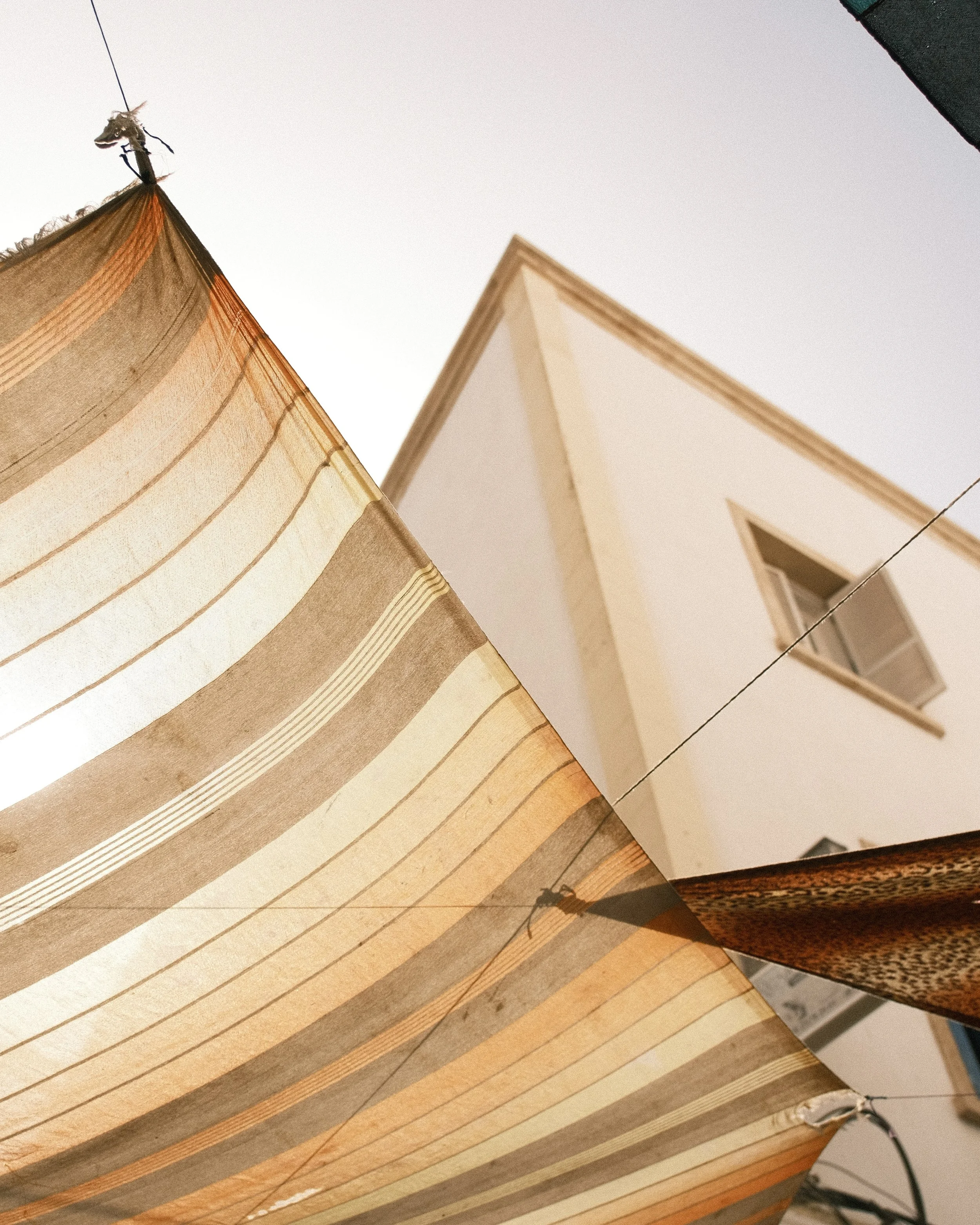 Une vue inclinée d'une maison blanche avec une fenêtre ouverte et des parasols en tissu rayé beige et orange.