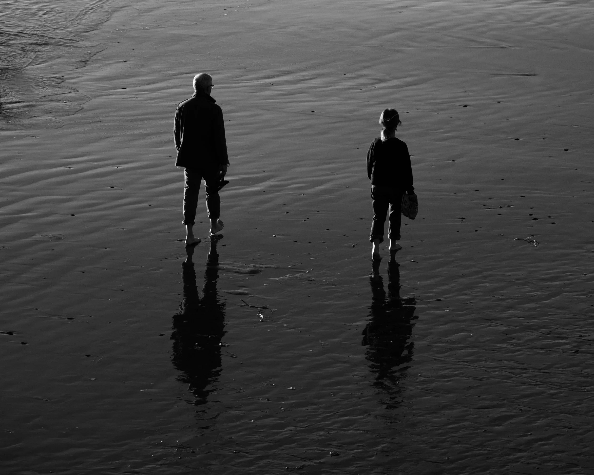 Deux personnes marchent dans la mer, vues de dos, en noir et blanc.