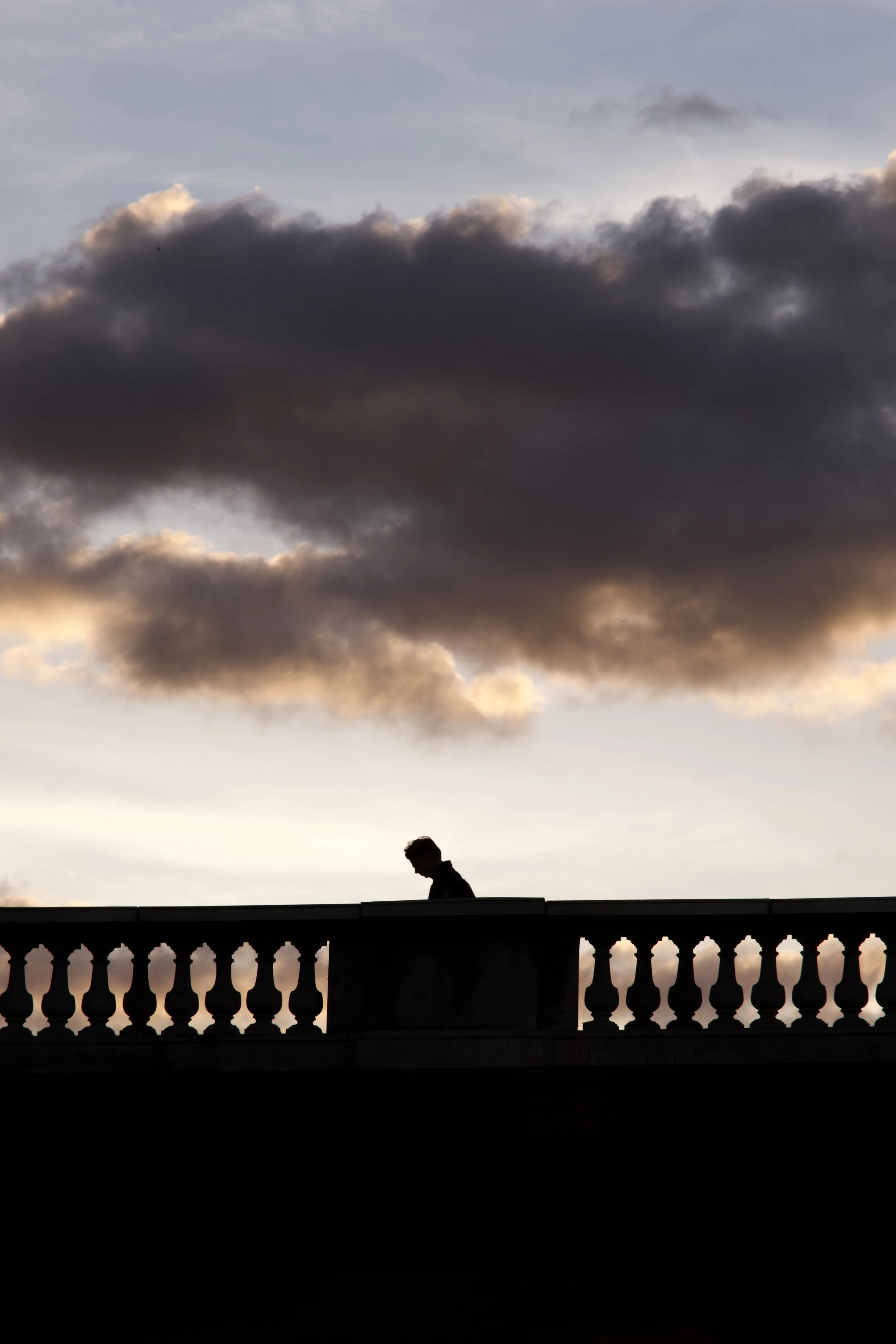 Silhouette d'une personne marchant sur un pont avec des nuages sombres dans le ciel au coucher du soleil.