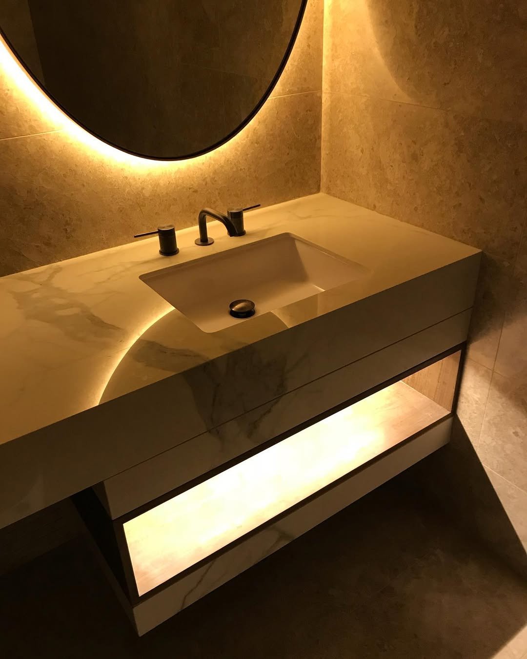 Modern bathroom vanity with a marble countertop, black fixtures, and backlit mirror with warm lighting.