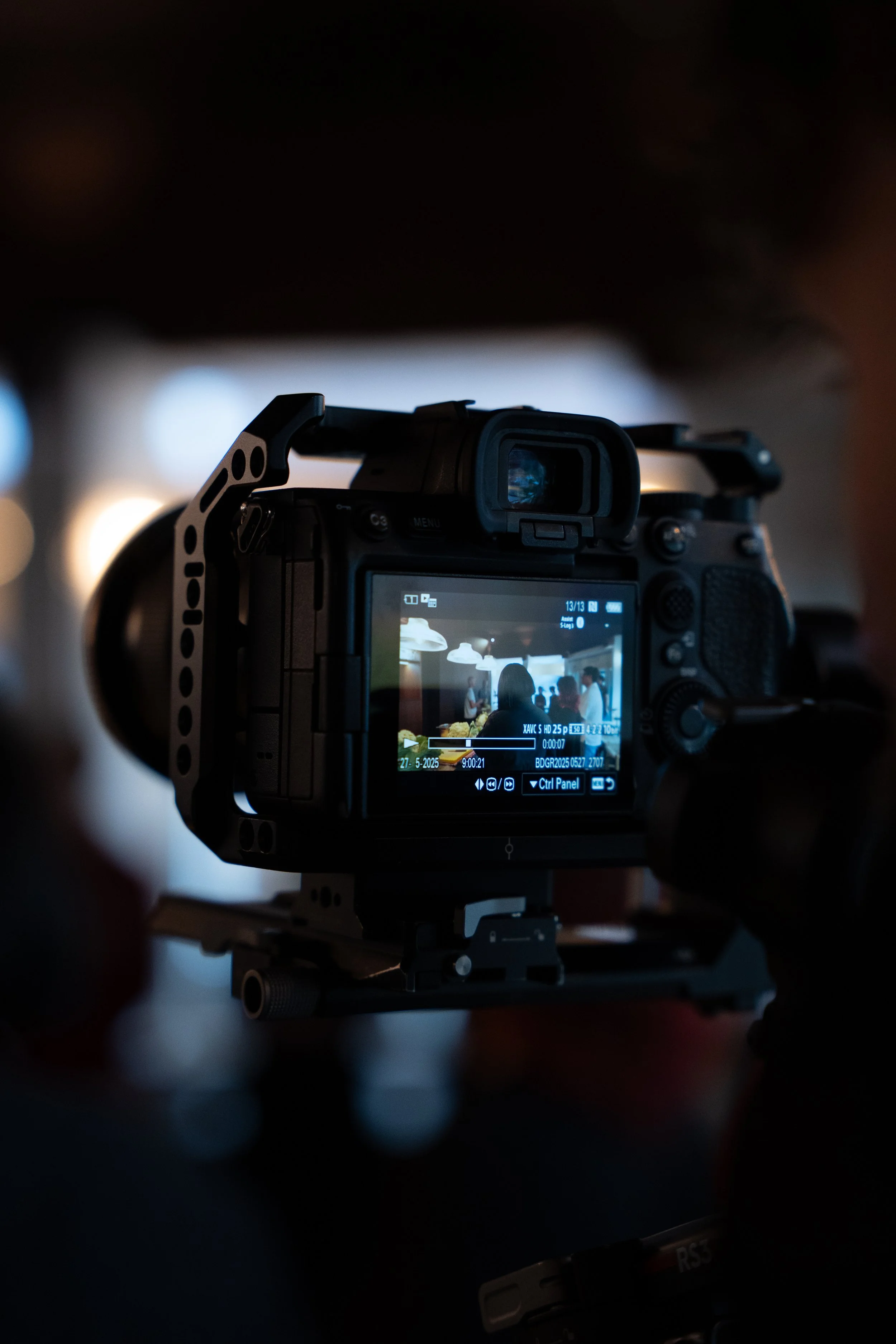 A digital camera on a tripod capturing a scene of people mingling in a room with hanging lights.