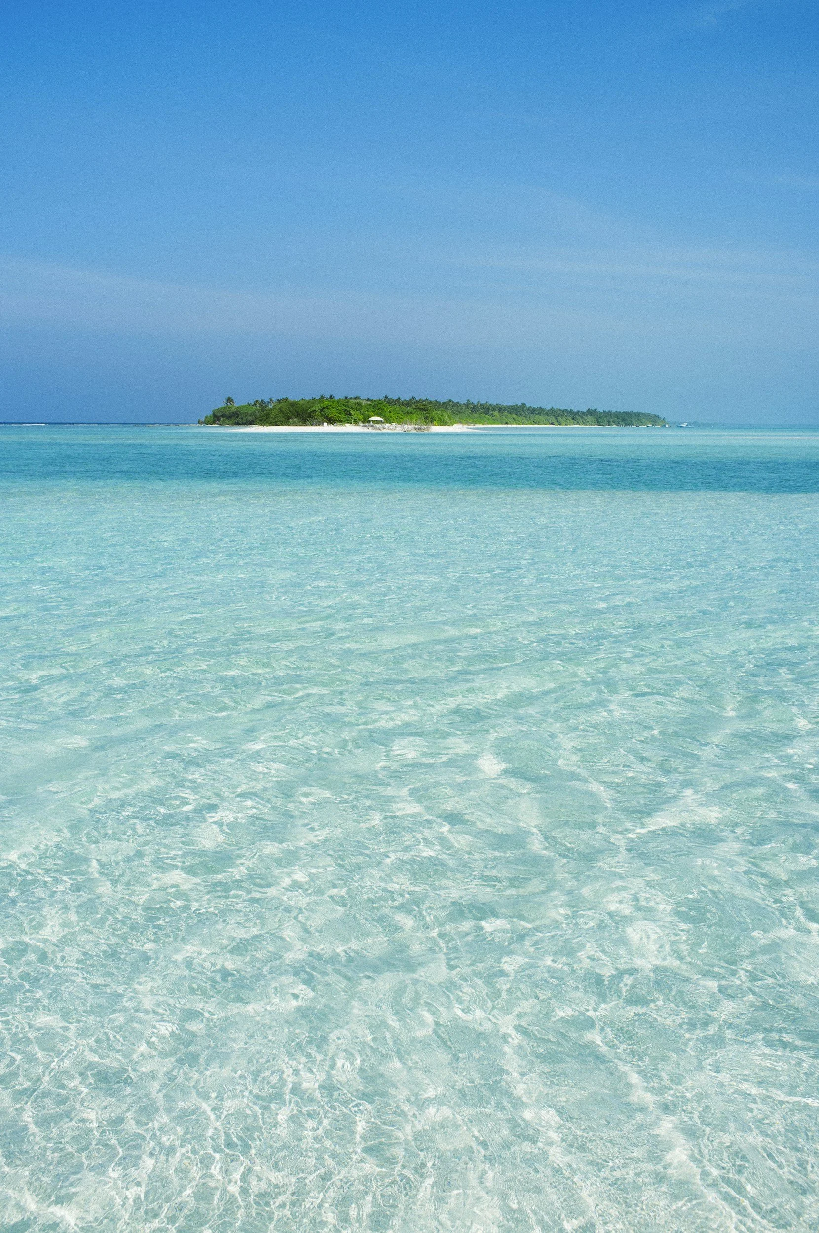 Clear turquoise water with a distant green island under a blue sky.