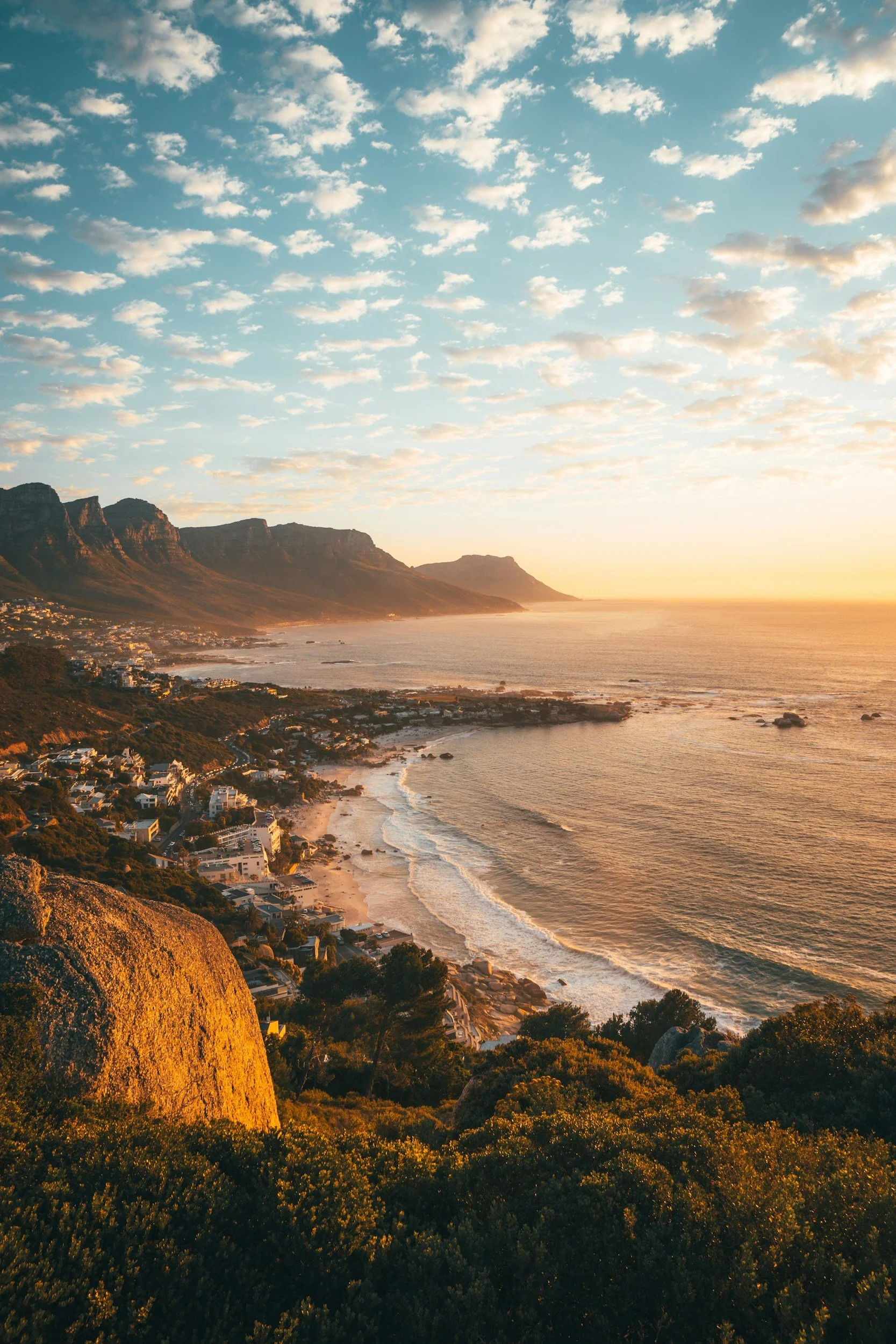 Scenic view of a coastline during sunset with mountains in the background, the ocean, and houses along the shore.