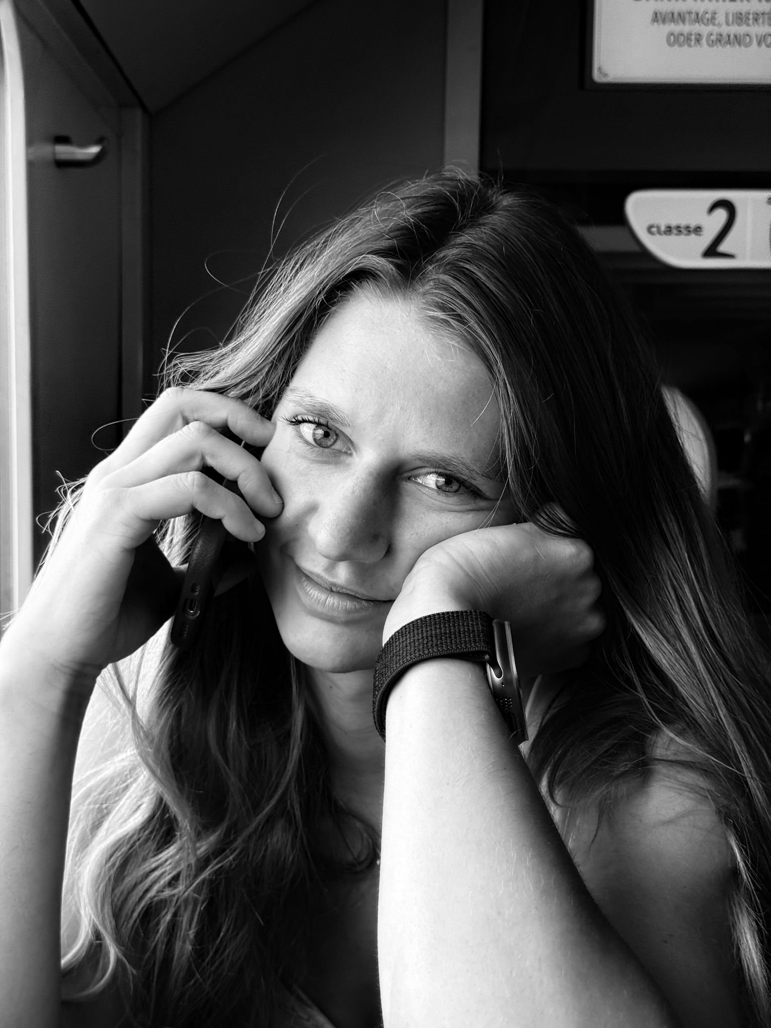 Das Bild zeigt eine junge Frau mit langen, gewellten Haaren, die im selben Moment telefoniert und entspannt in die Kamera blickt.