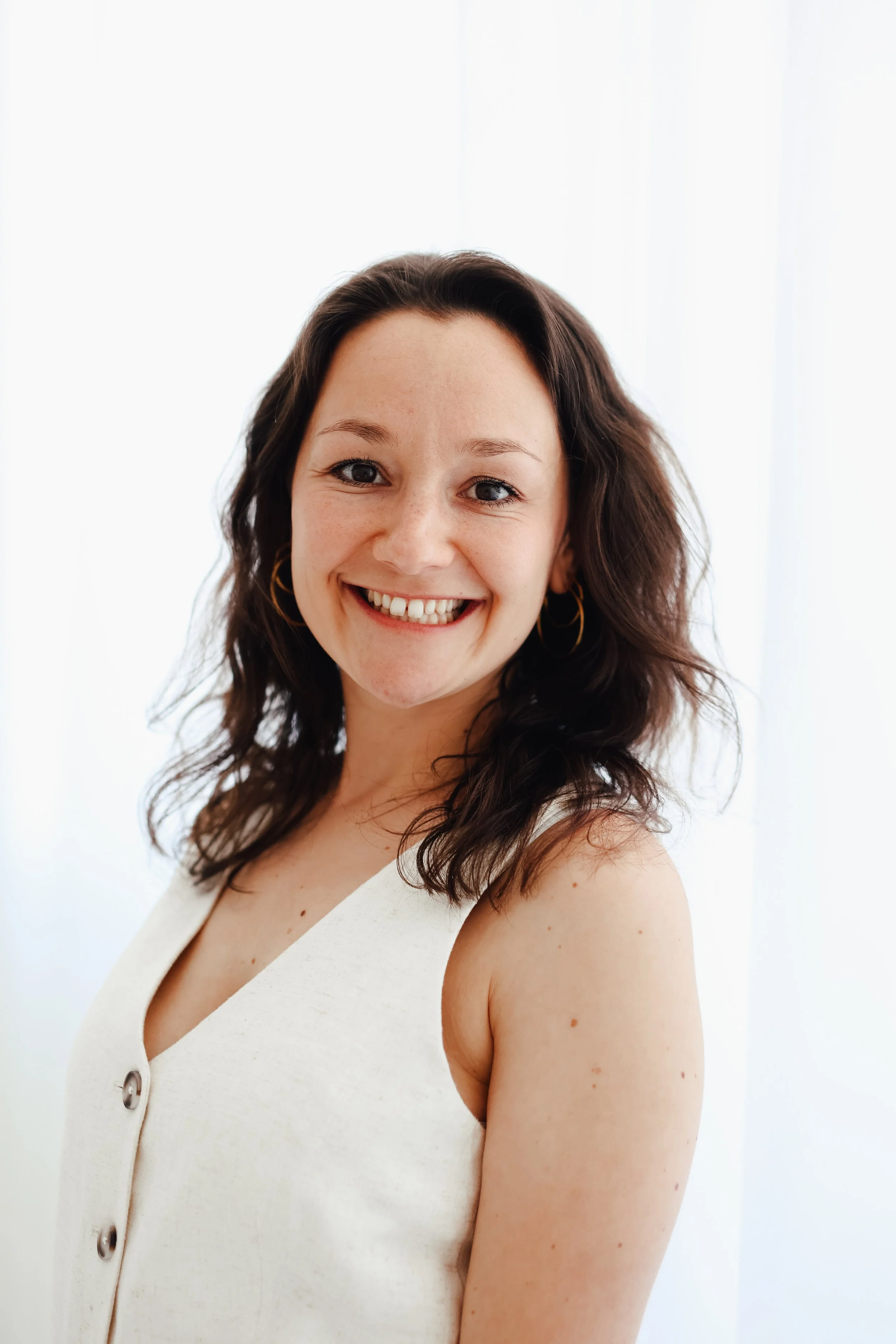 Felicia Thiering, systemische Beraterin & Elterncoach mit braunen, lockigen Haaren und Ohrringen, trägt weiße Kleidung, steht vor weißem Hintergrund.
