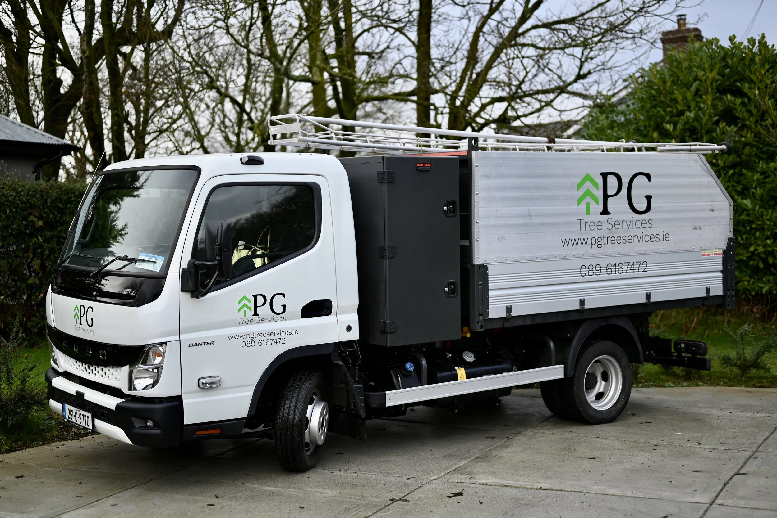 White truck labeled with 'PG Tree Services' parked on a driveway, with trees and bushes in the background.