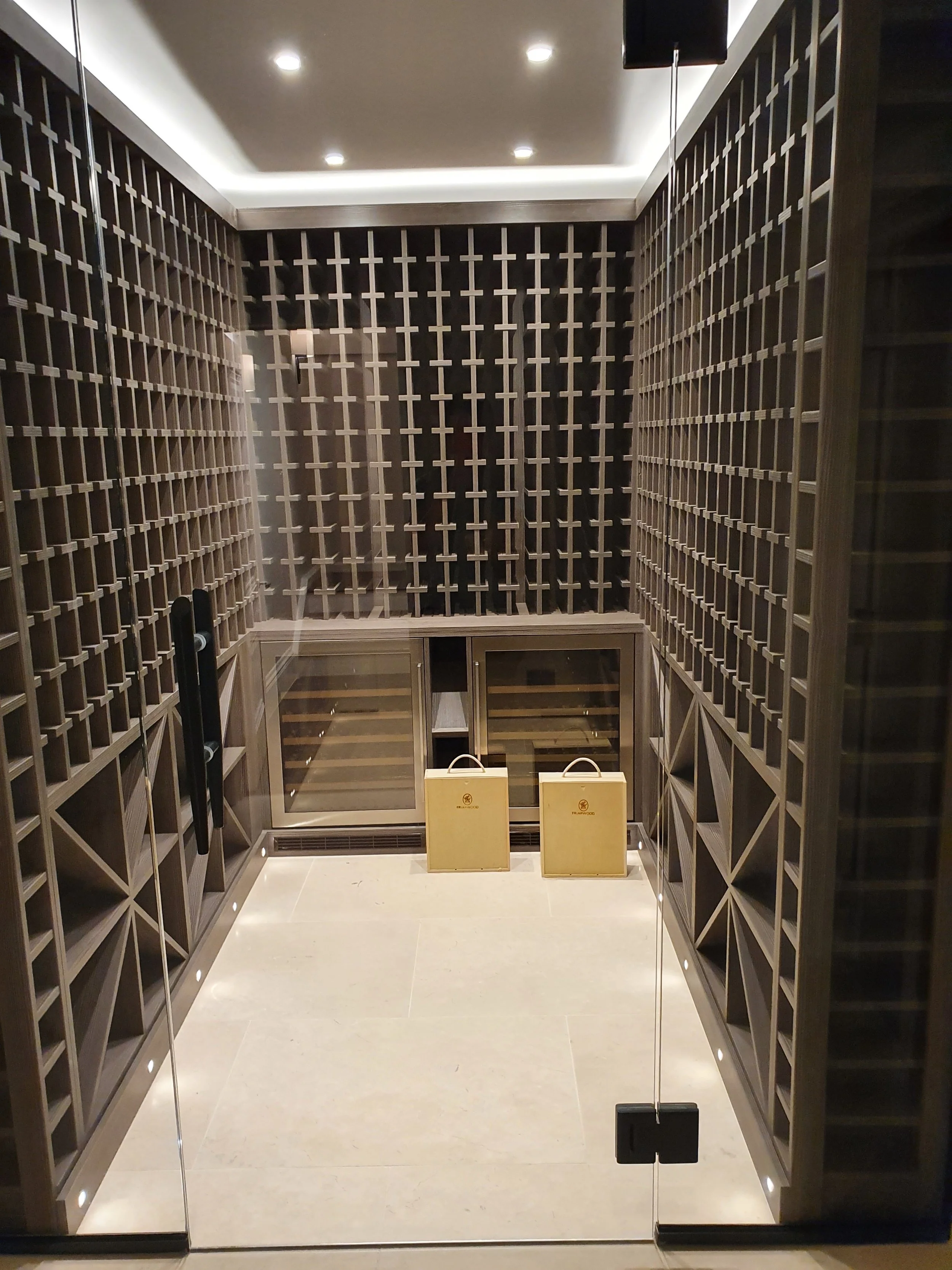 Luxury wine cellar with glass doors, wooden wine racks lining the walls, and two beige wine crates on the light-colored floor.