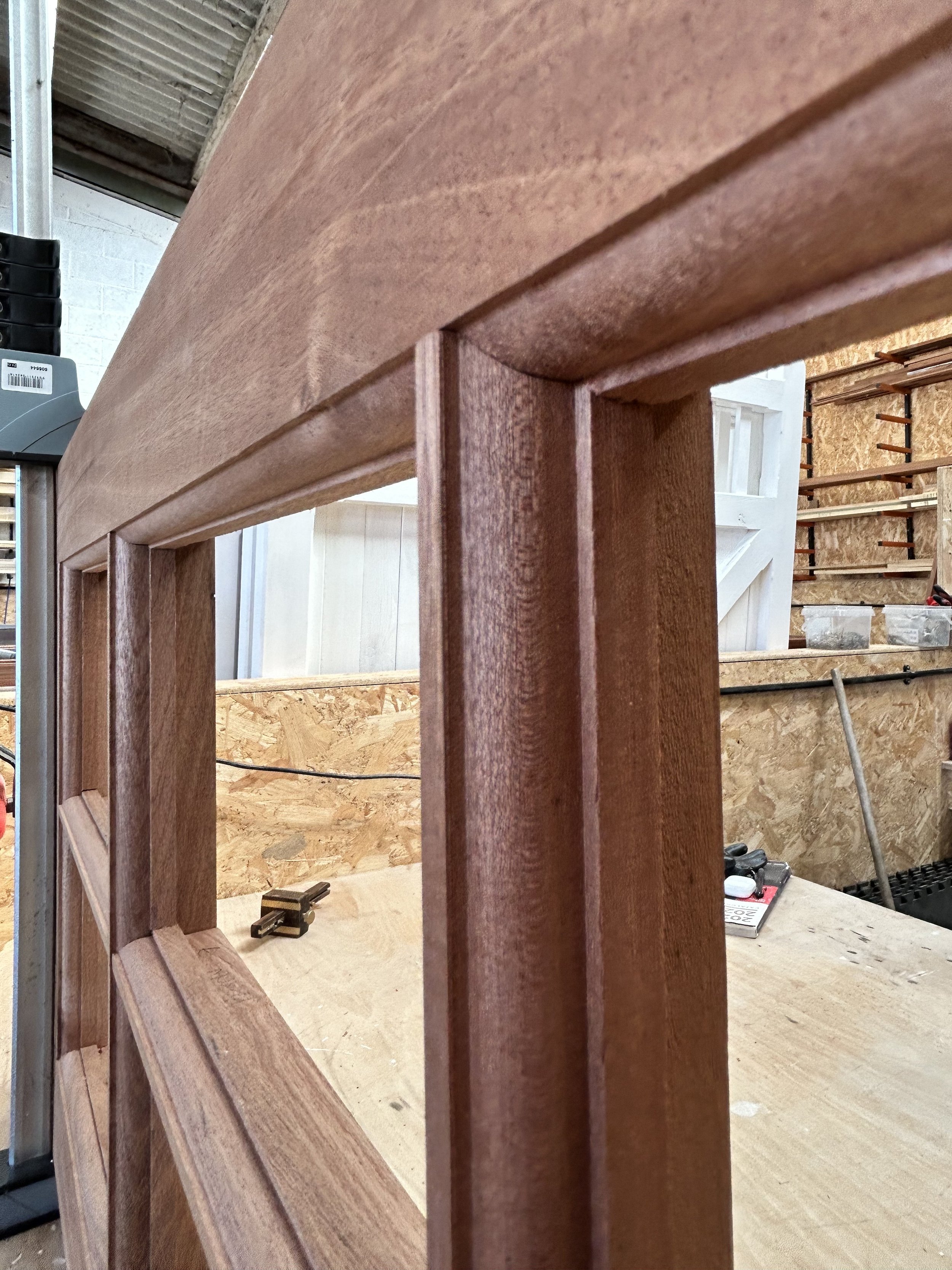 Close-up of a wooden window frame in a woodworking shop with tools and materials in the background.